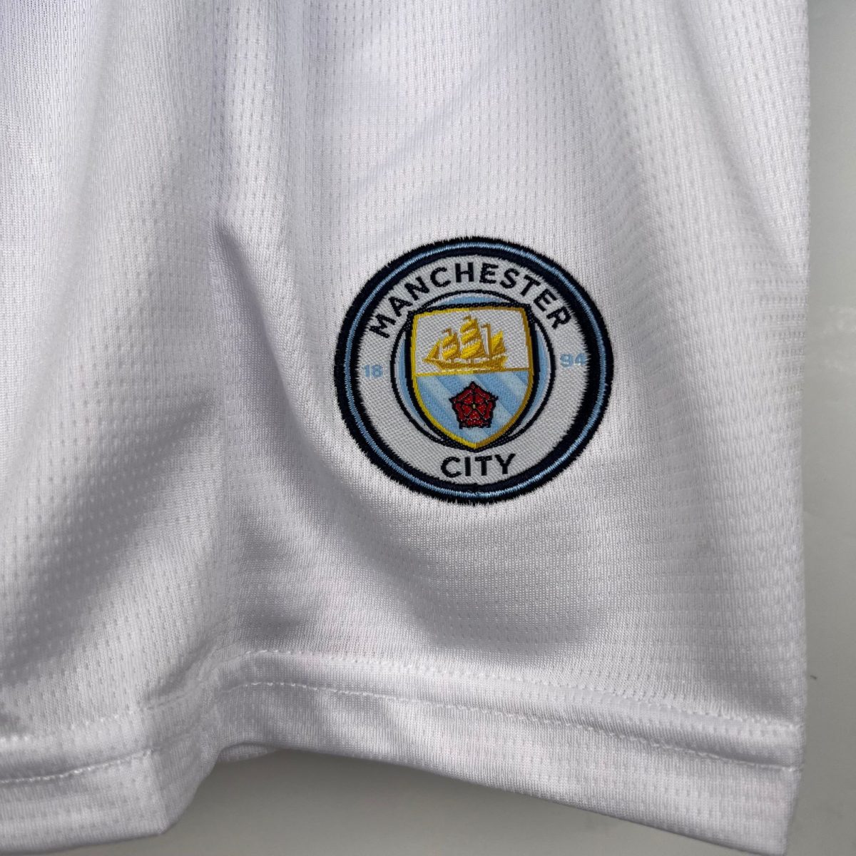 Close-up of white textured fabric featuring a circular embroidered Manchester City badge in blue, yellow, and light blue.