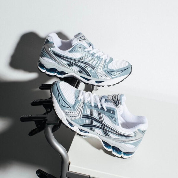 Pair of white and light blue running shoes with teal accents resting on a metal exercise stand.