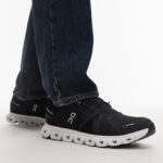 Black On running shoes with white segmented soles, worn with dark jeans, side view on a white background.