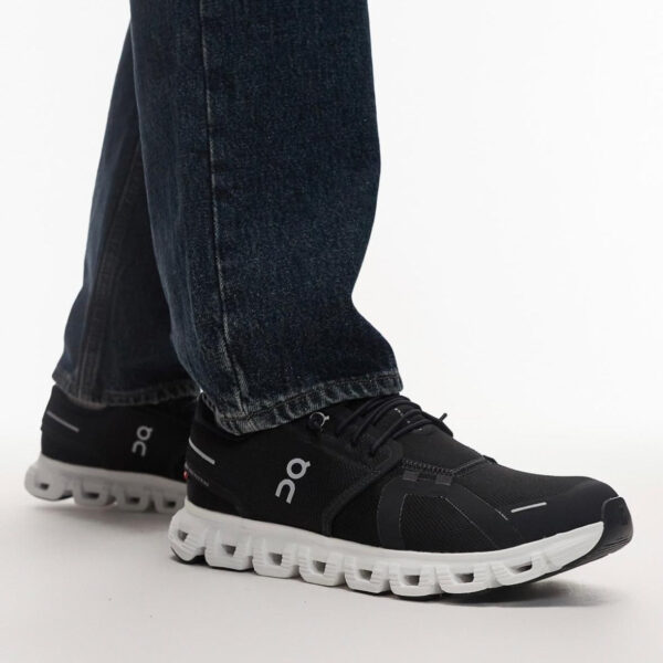 Black On running shoes with white segmented soles, worn with dark jeans, side view on a white background.