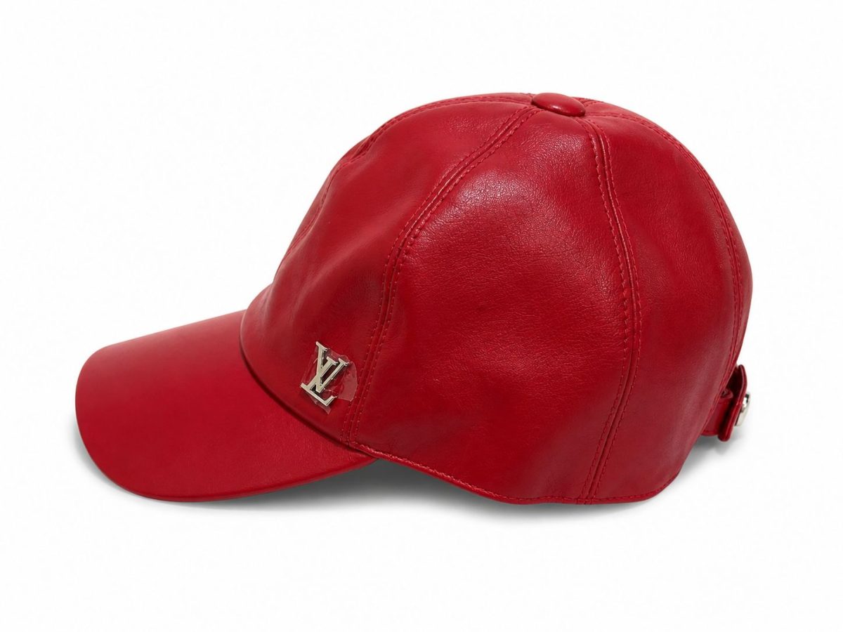 Red leather baseball cap with a silver LV logo on the front panel placed against a white background, side view.