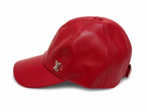 Red leather baseball cap with a silver LV logo on the front panel placed against a white background, side view.