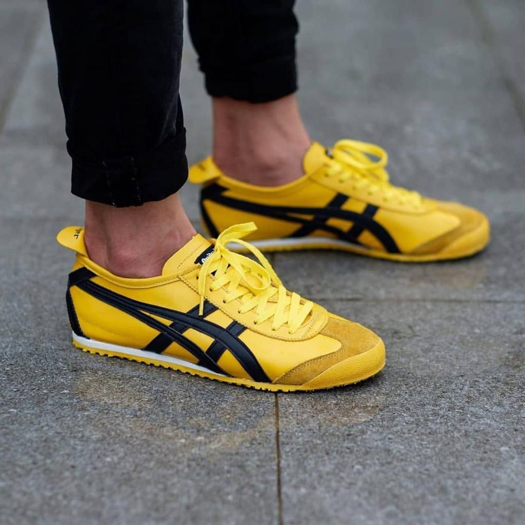 a81fe7f0-8b3c-4298-a0c4-f8ca289733d3_3ed18bc7-1d5a-45ec-a192-bec892096bfa Pair of bright yellow sneakers with black stripes resting on a gray pavement surface, laces tied.