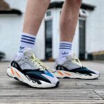 Pair of chunky running shoes with pale yellow laces, white socks with blue stripes, standing on a wooden deck.