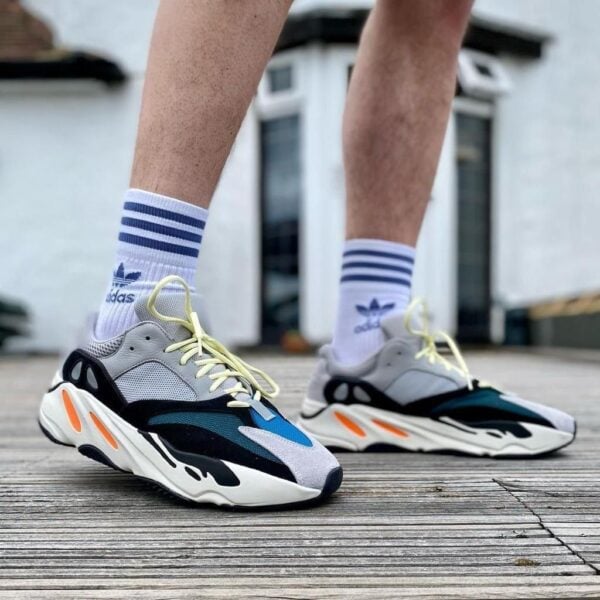 Pair of chunky running shoes with pale yellow laces, white socks with blue stripes, standing on a wooden deck.