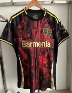 Front view of a black-and-red Bayer Leverkusen soccer jersey with gold 'Barmenia' sponsor, hanging on a wooden hanger.