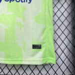 Close-up of a neon green sports jersey with a small black fabric tag reading 'ENGINEERED' and codes, on a metal mesh surface behind.