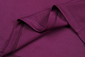 Close-up of burgundy fabric with a folded edge and visible stitching.