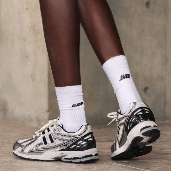 Person wearing white crew socks and gray-white running shoes standing on a concrete floor, angled legs visible