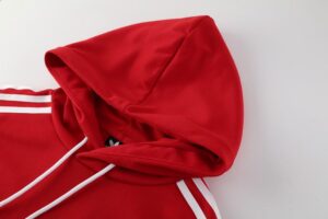 Red hoodie with white drawstrings and two white stripes along the sleeve on a light background, hood up