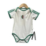 White baby onesie with green trim on sleeves and leg openings, hanging on a wooden hanger; circular patch with crescent and star on chest