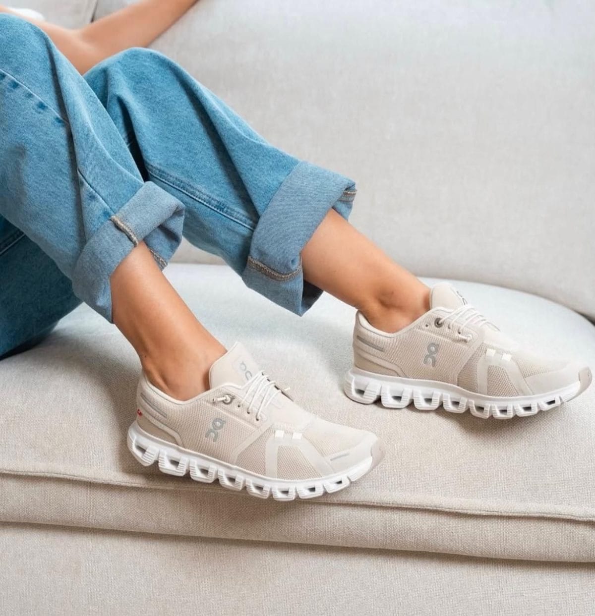 Person lounging on a sofa wearing light beige sneakers with rolled-up blue jeans.