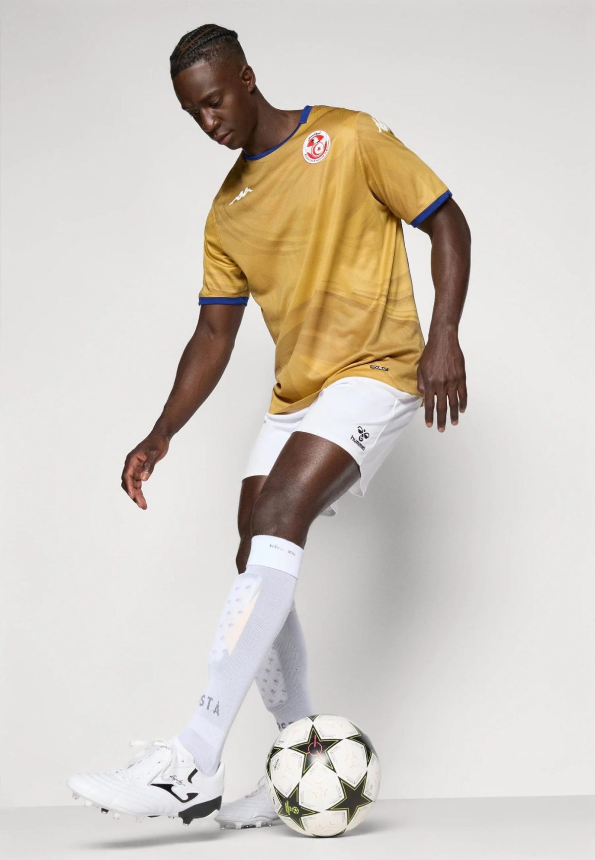 Soccer player in a gold jersey and white shorts dribbling a ball in a studio.