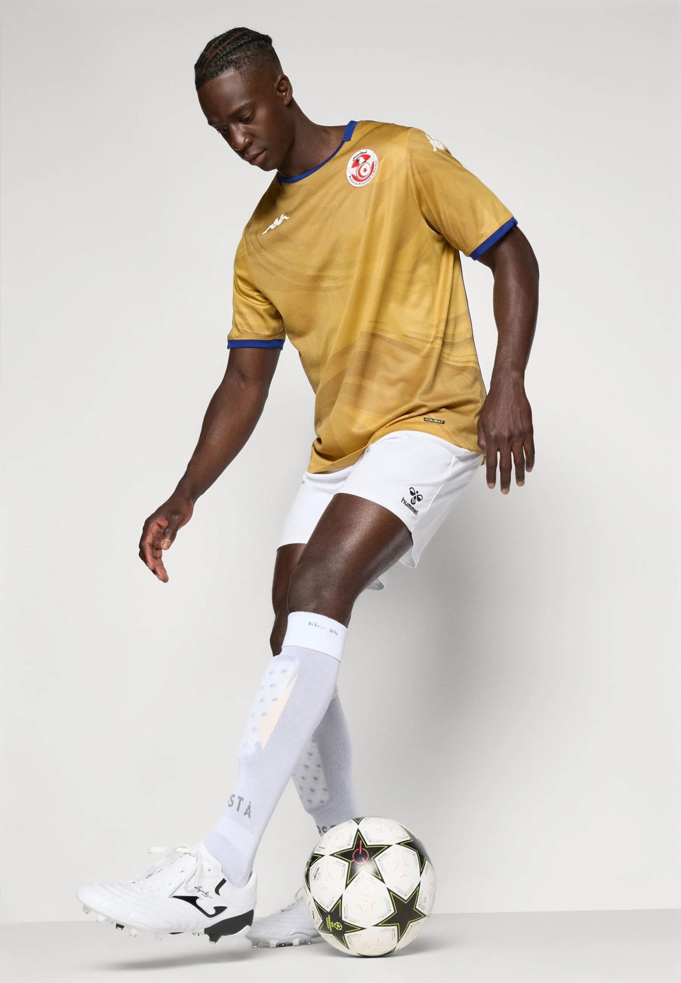 a9fdd37ad84c4f2c9cad425912dfd021 | UAE SPORT STORE Soccer player in a gold jersey and white shorts dribbling a ball in a studio.