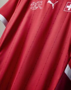 Close-up of a red sports jersey with white sponsor logos, including a Swiss cross badge and a Puma logo.