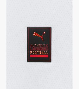 Black patch with red, metallic lettering reading 'AUTHENTIC LICENSED FOOTBALL' and a leaping red Puma logo on white fabric background.] , ...