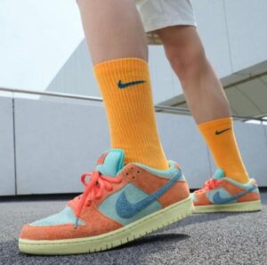 Colorful sneakers with turquoise swoosh, orange suede, and coral laces, paired with bright orange socks in a low-angle shot.