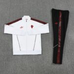 White zip-up athletic jacket with red logos next to black track pants with a red patterned side stripe, laid flat.
