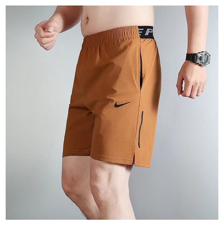 aa64fd2f | UAE SPORT STORE Man wearing brown athletic shorts with zip pockets and a black Nike swoosh logo.