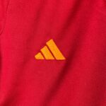 Close-up of red knit fabric with orange embroidered Adidas-style three stripes.
