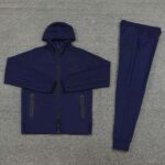 Navy blue Nike tracksuit laid flat on a gray carpet, jacket with zipper and matching pants on display.
