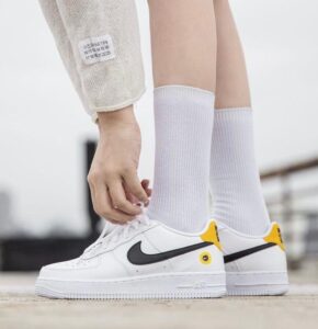 Close-up of a person tying white Nike sneakers with a black swoosh and yellow heel tabs, wearing white socks.