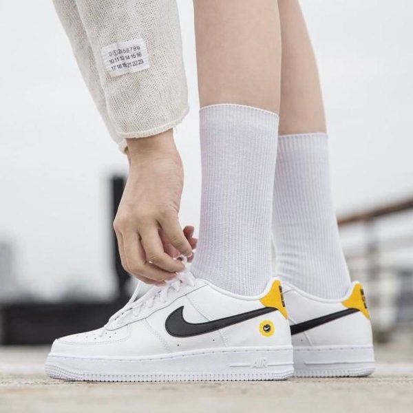 Close-up of a person tying white Nike sneakers with a black swoosh and yellow heel tabs, wearing white socks.