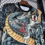 Black athletic jersey on a wooden hanger, featuring a blue-gold dragon graphic and a Japan JFA crest on the chest.