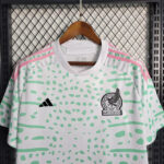 White Mexico soccer jersey with mint green abstract pattern, pink shoulder stripes, and Adidas logo on a hanger.