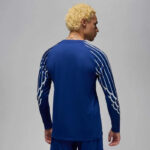 Back view of a person in a royal blue long-sleeve athletic shirt with white wing-like designs on the sleeves.