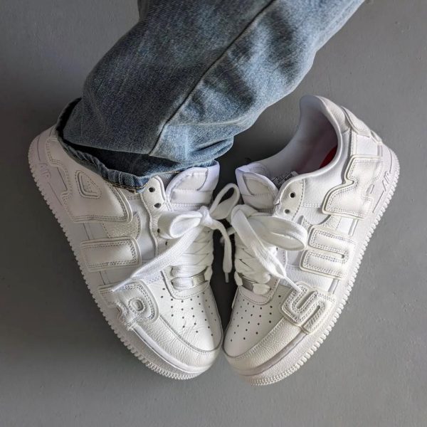 Top-down view of white sneakers worn with blue jeans, resting on a gray floor.