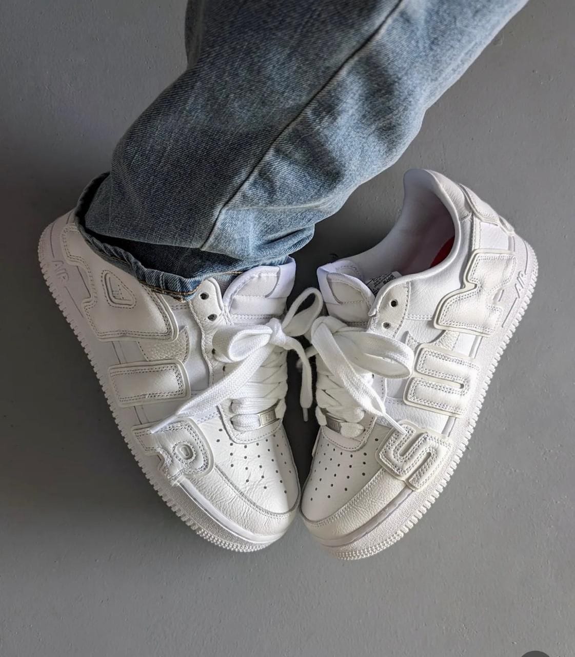 ab878a33-12e4-4a9e-9122-76238a0c811b Top-down view of white sneakers worn with blue jeans, resting on a gray floor.