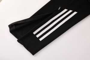 Close-up of black athletic pants leg with three white stripes along the side and a zipper at the ankle.