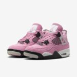 Pair of pink suede sneakers with black plastic eyelets and mesh panels, white midsole, and light-gray outsole, shown side by side.