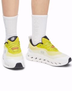 ac768573-7bad-4268-8532-3520aea43936 | UAE SPORT STORE Yellow athletic sneakers with a chunky white sole on both feet, paired with white crew socks and black heel accents on the shoes.