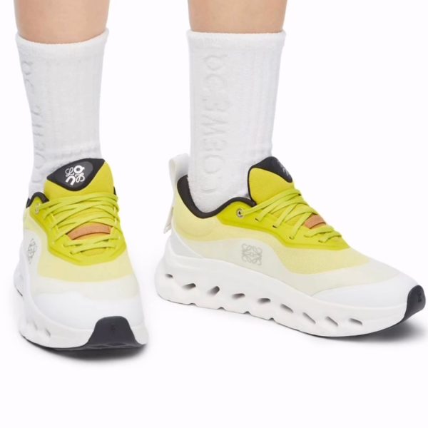 Yellow athletic sneakers with a chunky white sole on both feet, paired with white crew socks and black heel accents on the shoes.