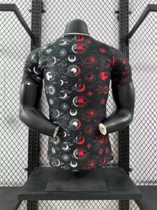 Back view of a black T-shirt with white and red celestial patterns on a mannequin, against a metal grid display.