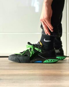 Close-up of a person tying bright green laces on black athletic sneakers with a speckled sole and green heel pods.