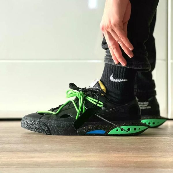 Close-up of a person tying bright green laces on black athletic sneakers with a speckled sole and green heel pods.