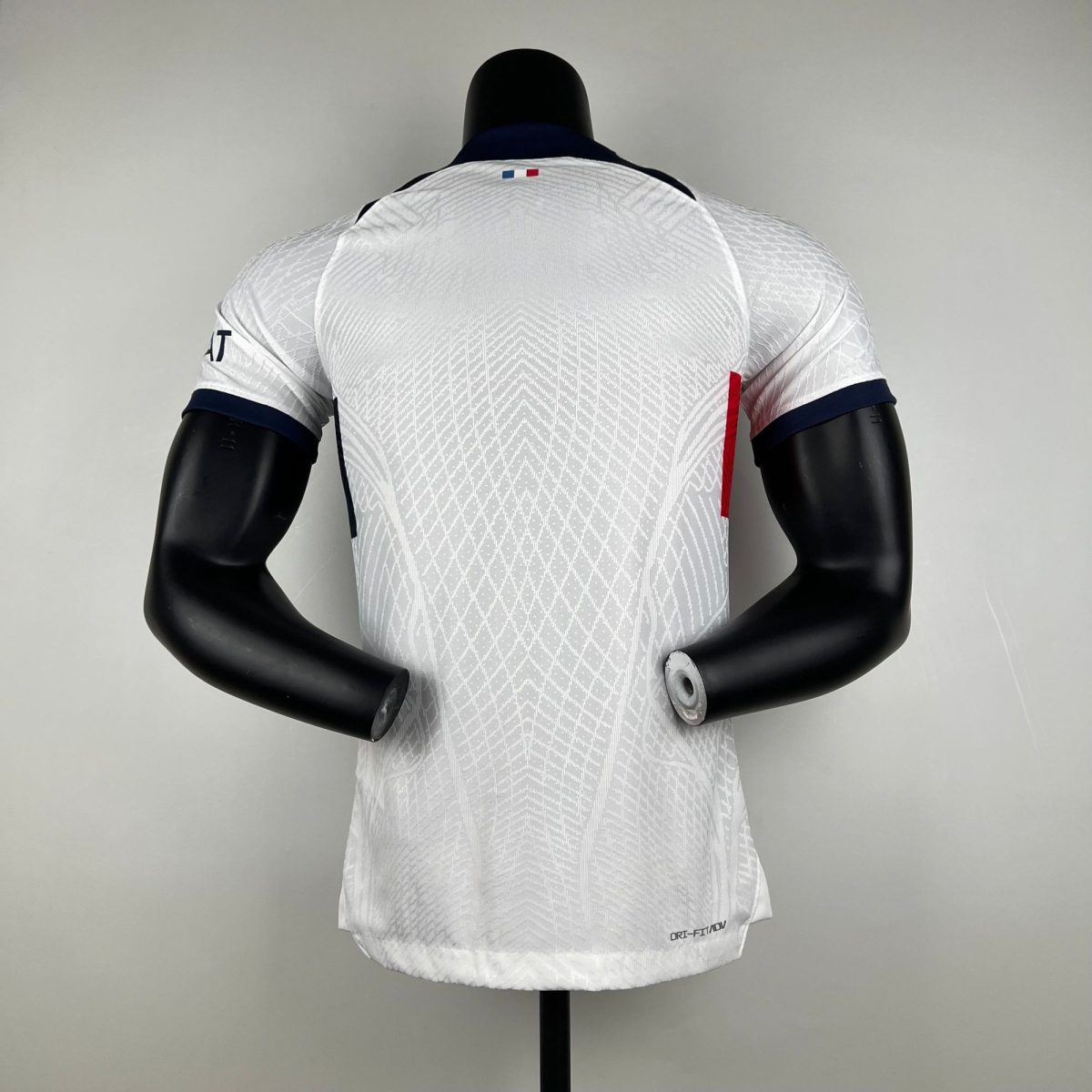 Back view of a white patterned sports jersey on a black mannequin torso, small French flag at the neckline.