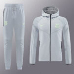 Light gray Barcelona training tracksuit—zip-up jacket with neon Nike swoosh and club crest, paired with matching jogger pants with drawstring.