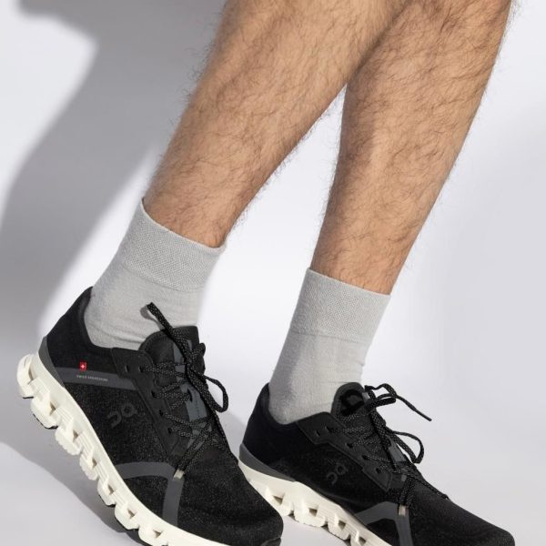 Black athletic sneakers with chunky white soles on a person wearing light gray socks, mid-step pose against a light background.