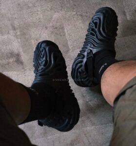 ad95717a-3570-47f7-b152-a143f1b6332d | UAE SPORT STORE Top-down view of two black chunky-soled sneakers worn with black socks on a concrete floor