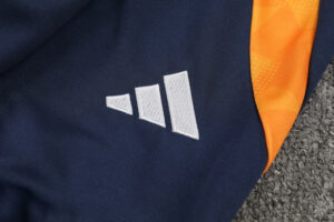 Close-up of navy fabric with the white Adidas three-stripe logo and an orange seam accent.