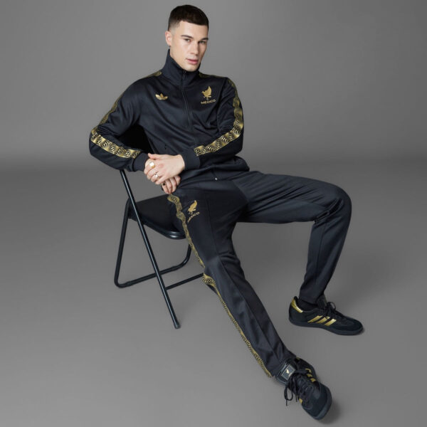 Man in a black tracksuit with gold detailing sitting on a folding chair, facing the camera.