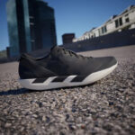 Black athletic sneaker on rough pavement with a modern cityscape in the blurred background.