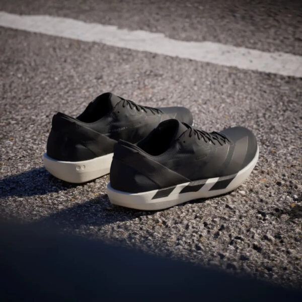Pair of black athletic sneakers with white soles resting on a paved surface, featuring diagonal stripes on the midsole edge.