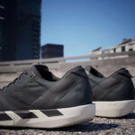 Pair of dark gray sneakers with white soles resting on a rooftop, urban cityscape in the background.
