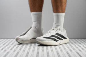 Person wearing white athletic socks and white sneakers with black stripes, standing on a patterned floor.