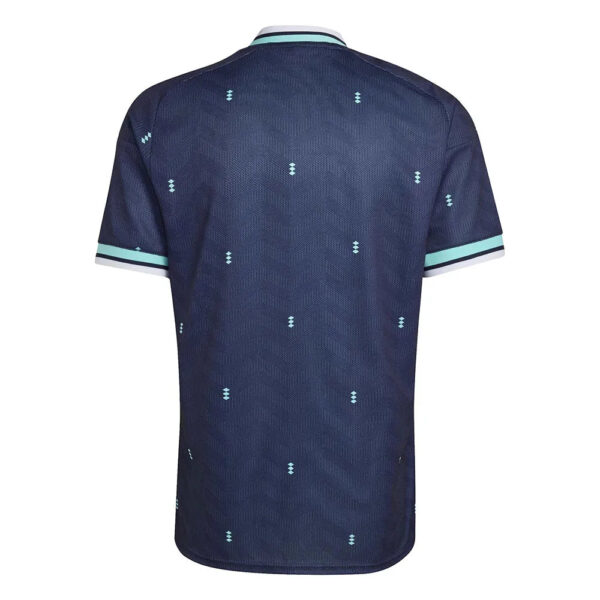 Back view of a navy polo shirt with small light-blue diamond patterns and mint trim on the collar and sleeves.”] ,